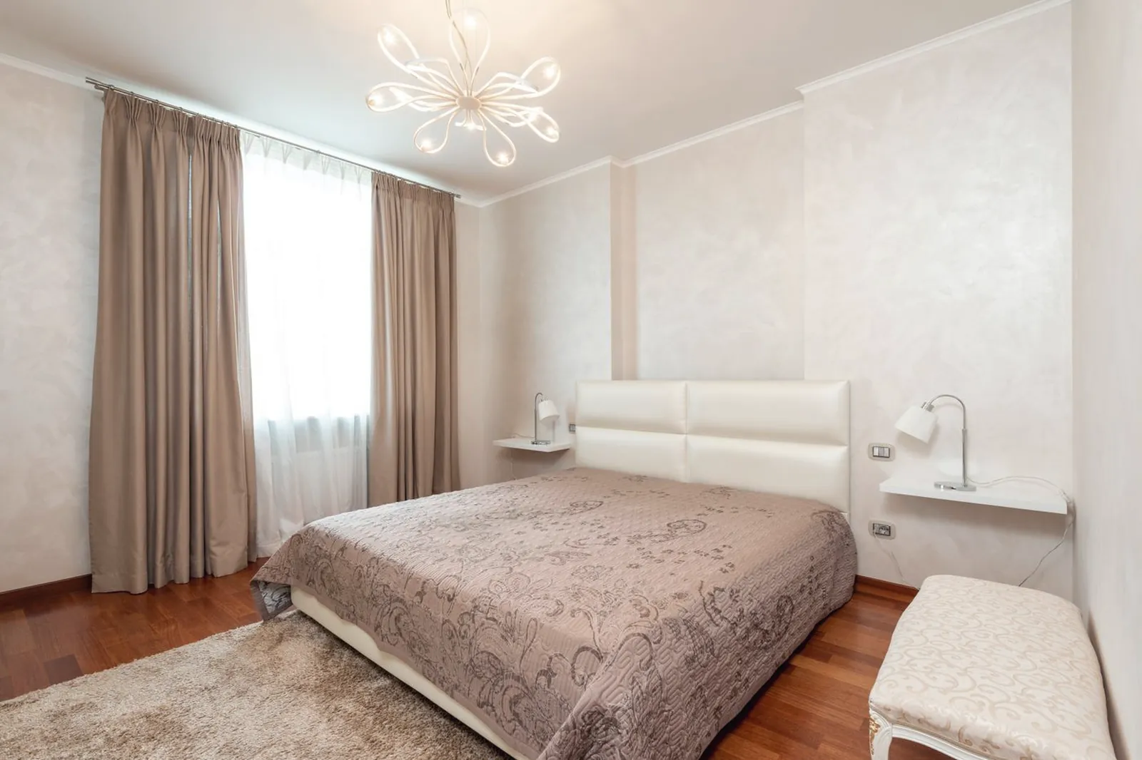 Chambre d’appartement classique avec lit double, rideaux clairs et lustre