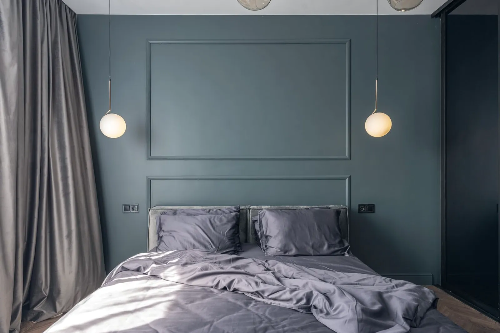 Chambre aux murs sombres avec un lit défait, éclairée par deux suspensions