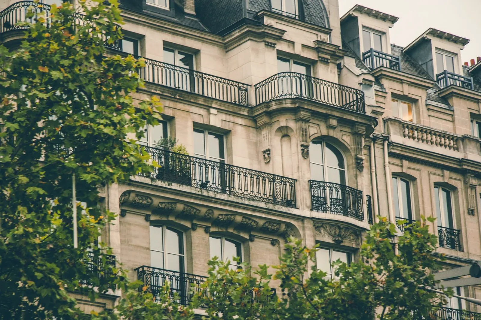 Façade haussmannienne aux balcons ouvragés, encadrée par des arbres