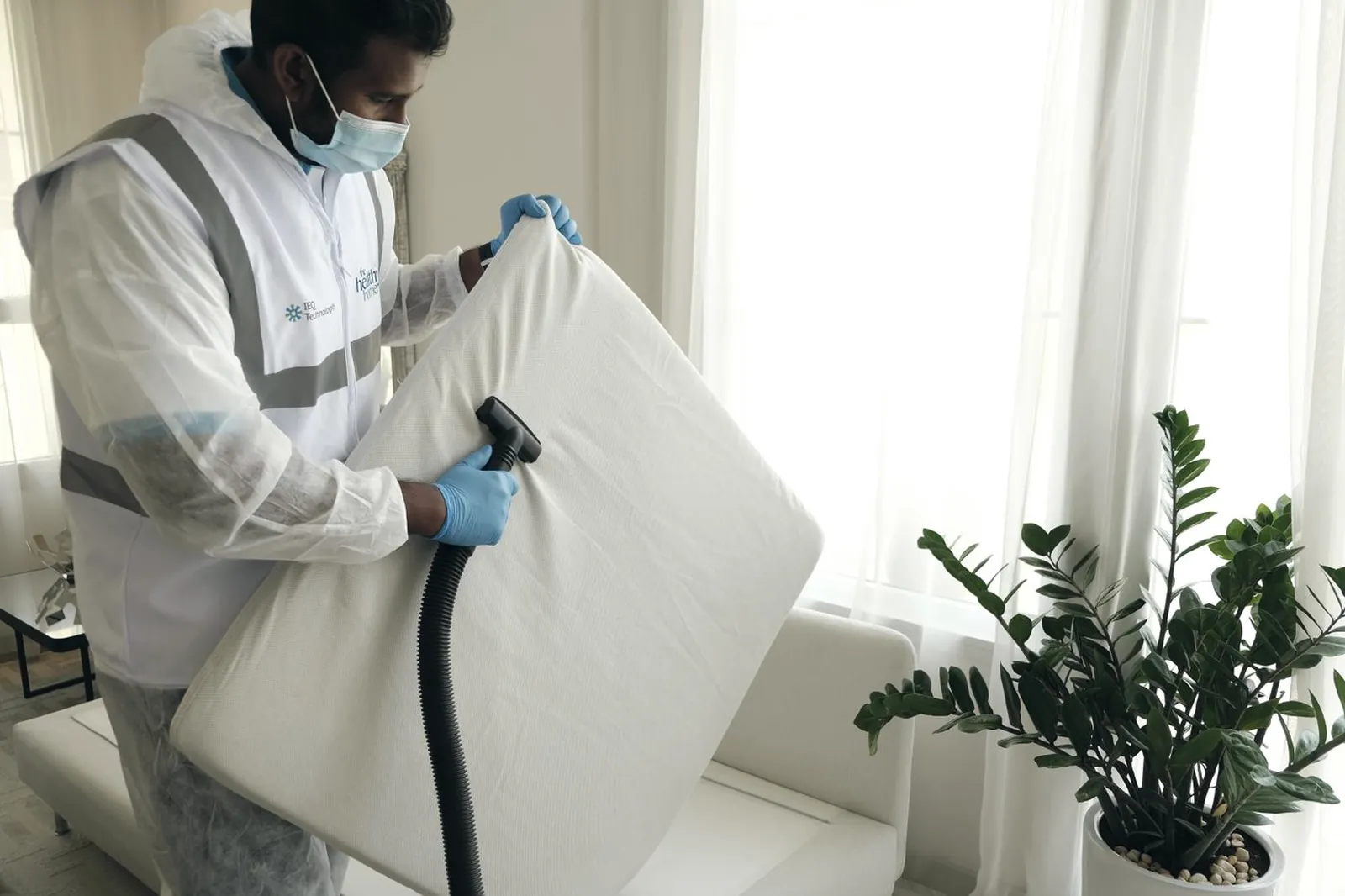 Technicien en combinaison de protection et masque nettoyant un matelas à l’aspirateur dans une chambre claire